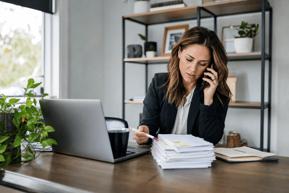 A real-estate agent on the phone at her desk with a stack of unconverted lead notes.