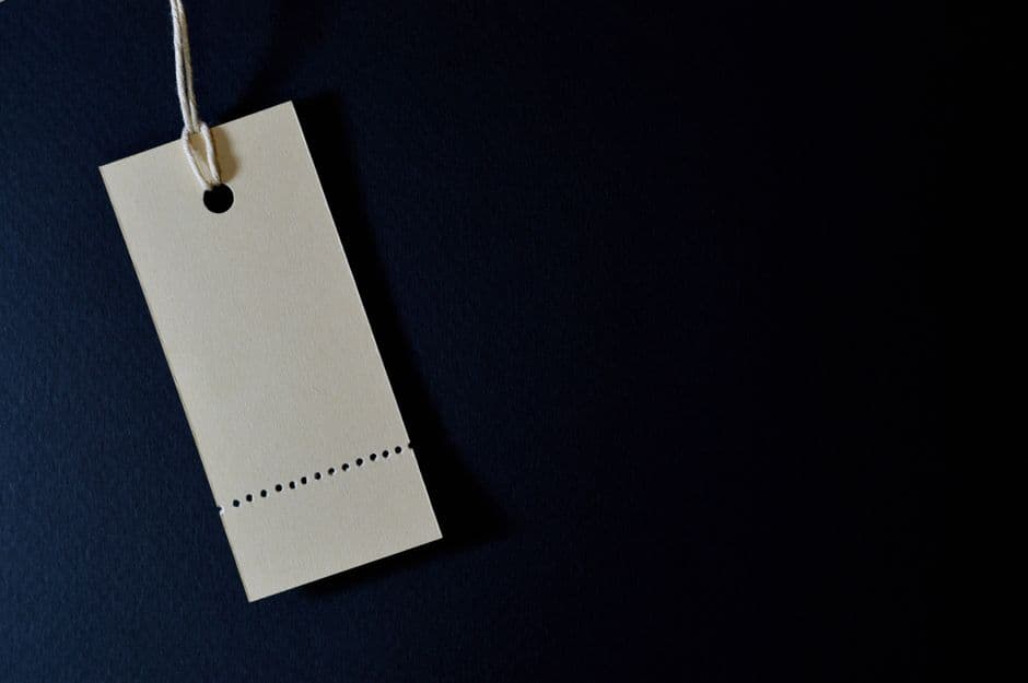 A single blank cream price tag hangs by a string against a deep navy background, lit to look premium and minimal.