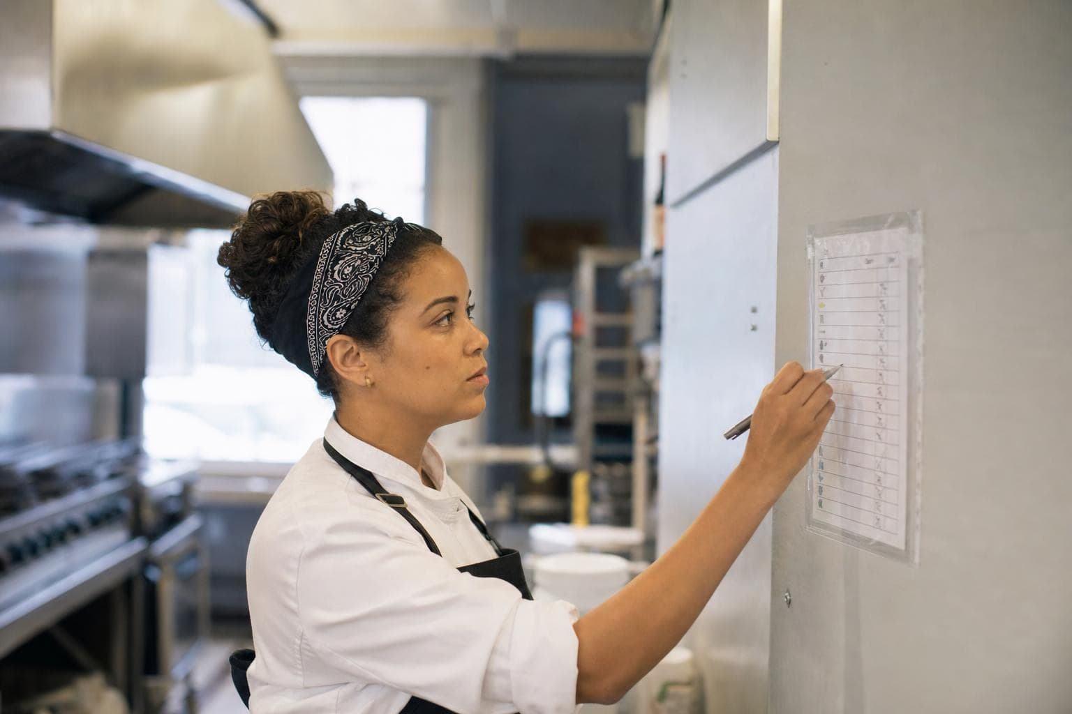 A commercial-kitchen owner checking items off a laminated checklist on the wall.