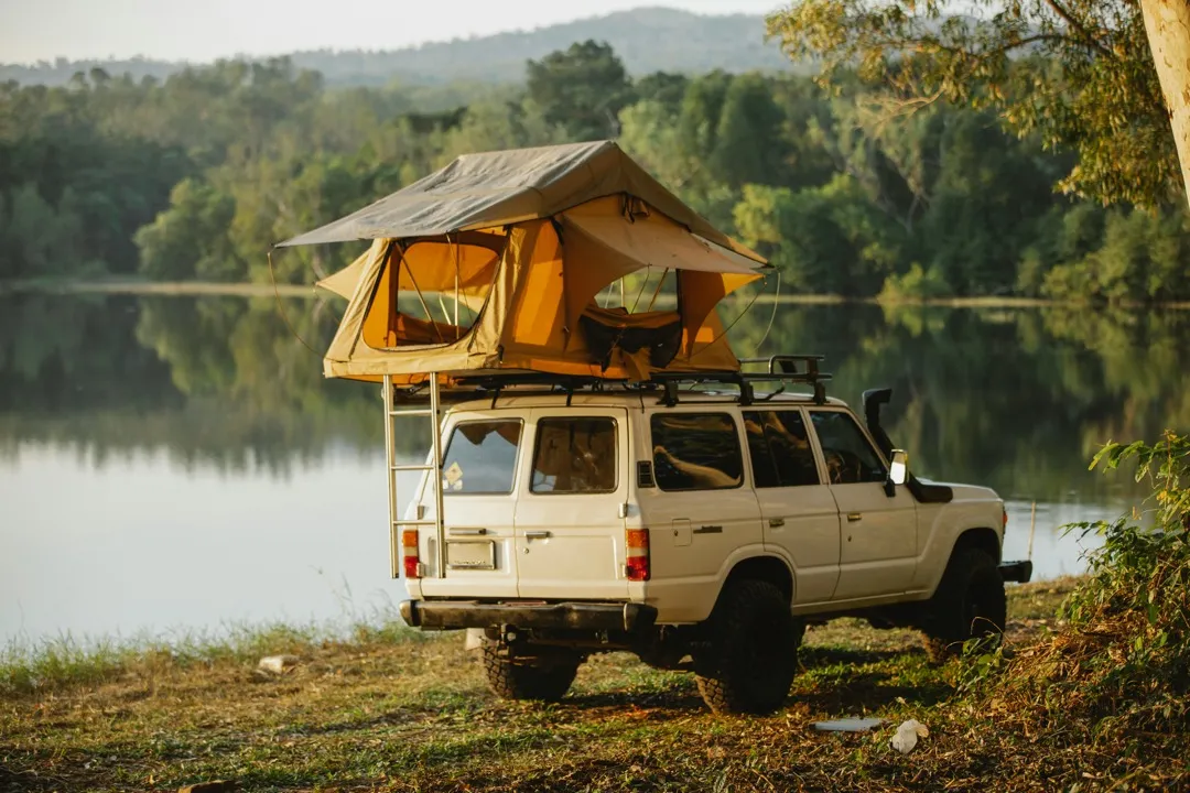 A rooftop-tent four-wheel drive parked beside a still lake at golden hour