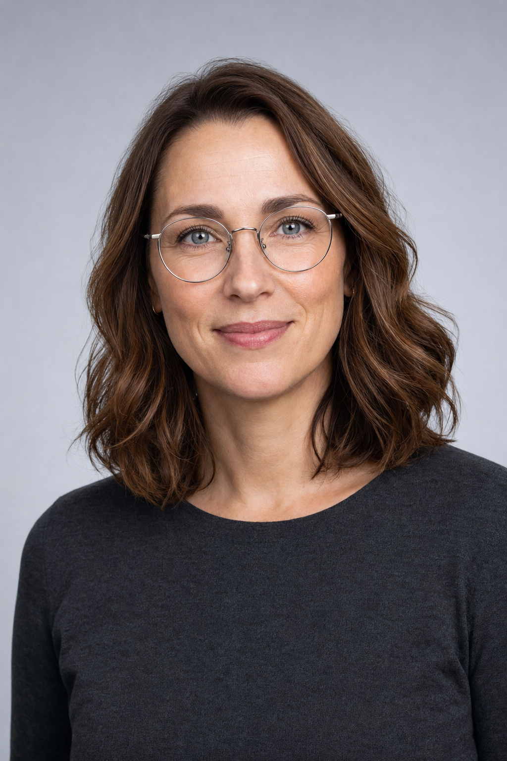 Dr. Nora Kessler, optometrist and founder, in round thin-rim glasses against a cool grey backdrop.